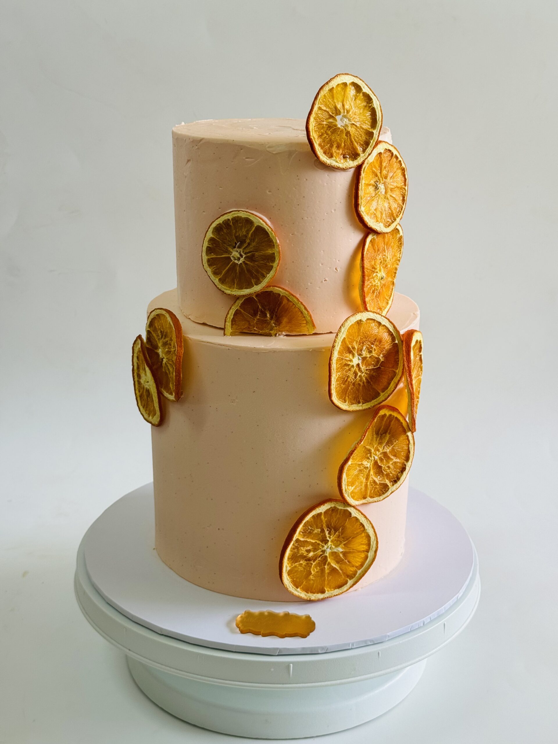 Bespoke two-tier buttercream cake with dried orange slices and neutral textured finish, custom celebration cake in Ayr.