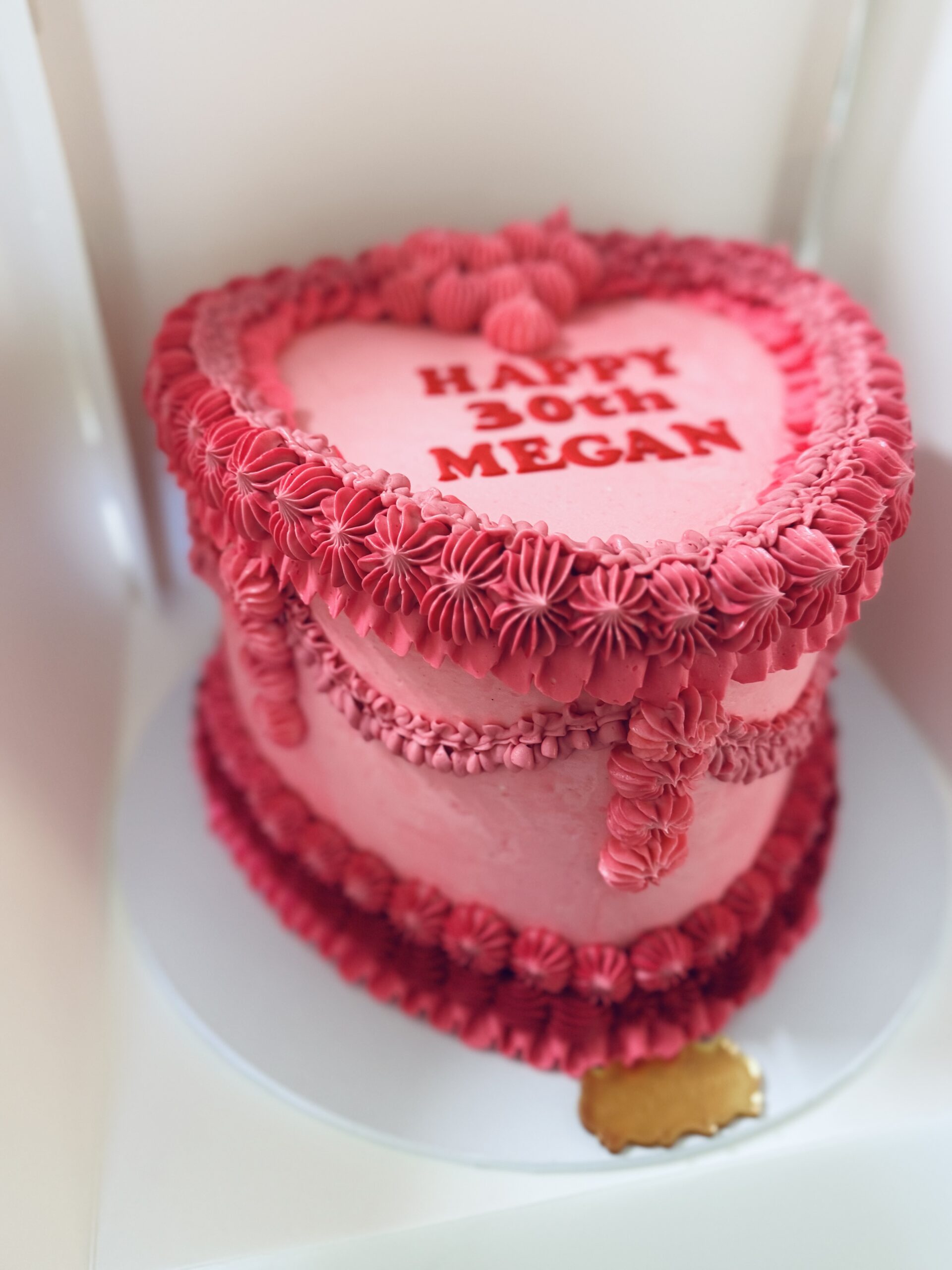 Custom heart-shaped pink buttercream birthday cake with piped border detail and personalised message.